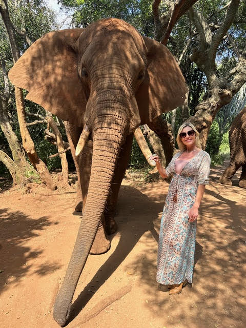 Kristin, a woman, standing next to an elephant while in an african lanscape