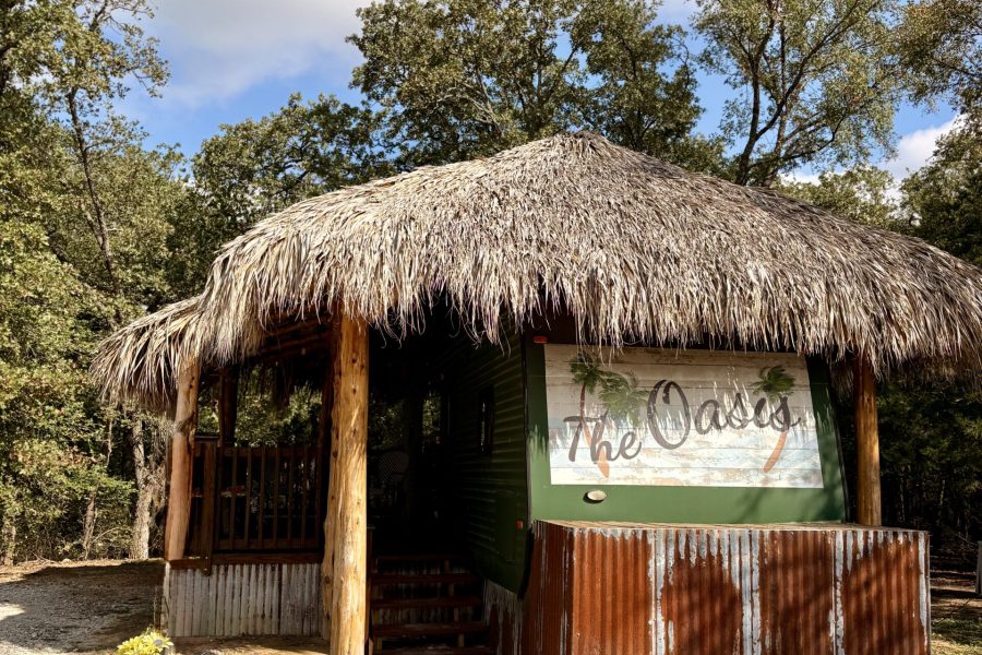 Outdoor view of a rustic rv called The Oasis with an additional straw roof and patio area